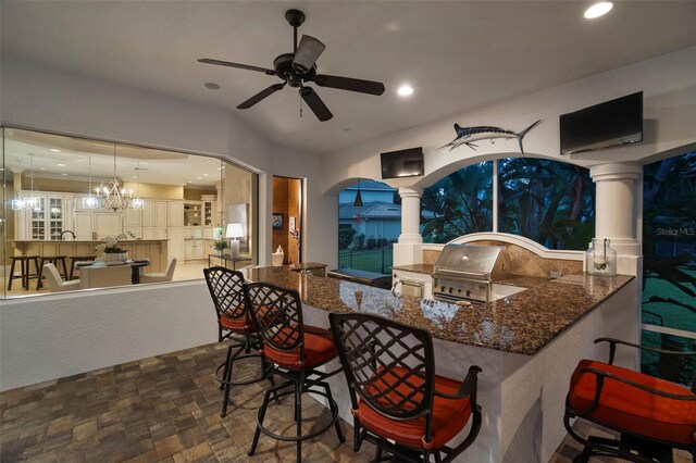 kitchen with decorative light fixtures, ceiling fan with notable chandelier, tasteful backsplash, dark tile flooring, and a breakfast bar