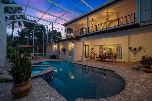 pool at dusk with an in ground hot tub, a lanai, central air condition unit, and a patio