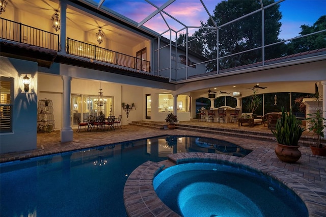 pool at dusk featuring glass enclosure, an in ground hot tub, a patio area, and ceiling fan