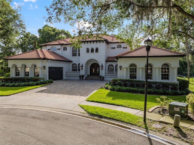 mediterranean / spanish-style home with a garage, decorative driveway, stucco siding, and a tile roof