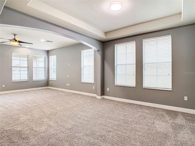 empty room with carpet floors, a tray ceiling, and ceiling fan