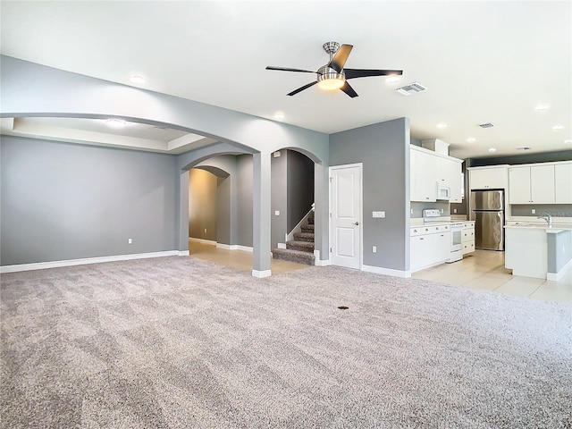 unfurnished living room featuring light colored carpet, ceiling fan, and sink