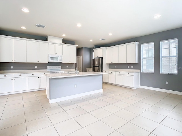 kitchen with sink, light tile patterned floors, white appliances, a kitchen island with sink, and white cabinets