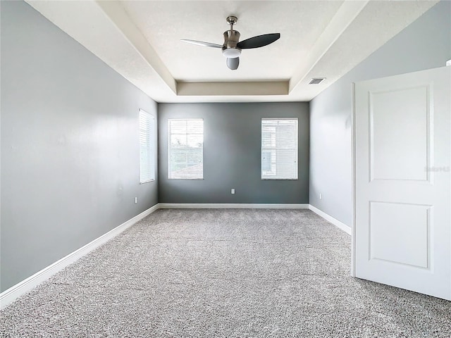 carpeted empty room with ceiling fan and a raised ceiling