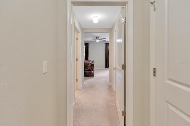 hallway with light carpet and a textured ceiling