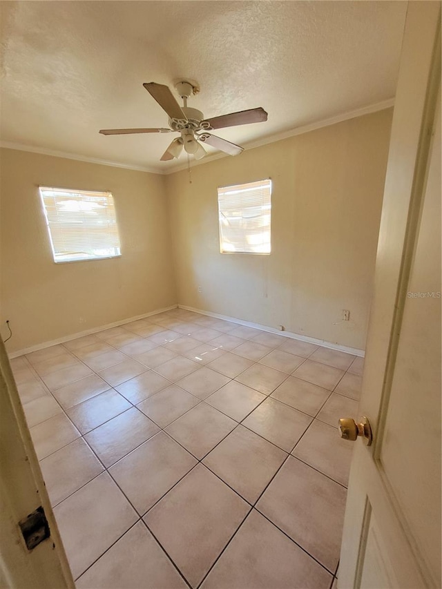 empty room with a textured ceiling, ceiling fan, light tile patterned flooring, baseboards, and crown molding