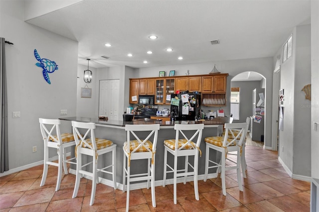 kitchen with visible vents, arched walkways, brown cabinets, a kitchen breakfast bar, and black appliances