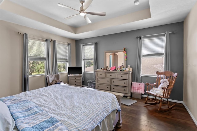 bedroom featuring dark wood-style floors, baseboards, a tray ceiling, and a ceiling fan