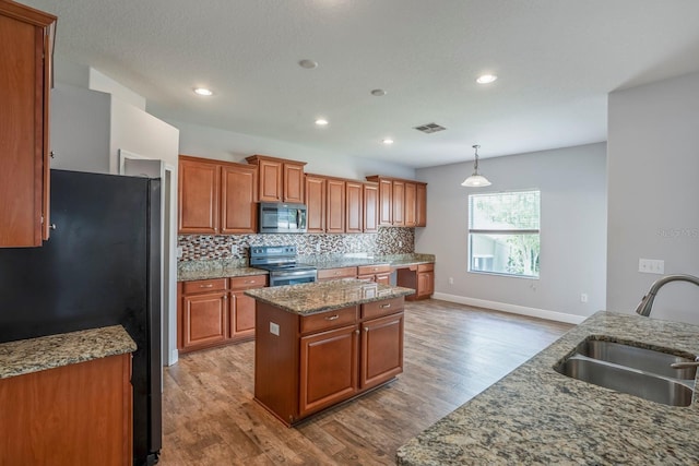 kitchen with a kitchen island, appliances with stainless steel finishes, decorative light fixtures, sink, and light hardwood / wood-style floors