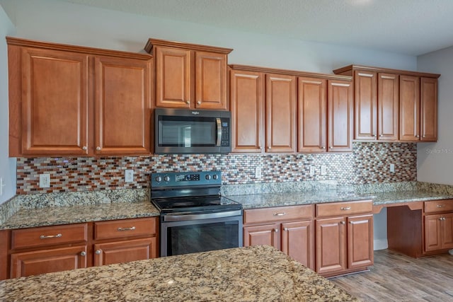 kitchen featuring stainless steel appliances, light stone counters, built in desk, light hardwood / wood-style floors, and decorative backsplash