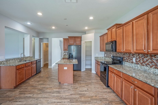 kitchen featuring sink, light hardwood / wood-style flooring, a kitchen island, light stone countertops, and black appliances