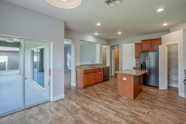 kitchen with sink, wood-type flooring, stainless steel fridge with ice dispenser, dishwashing machine, and light stone countertops