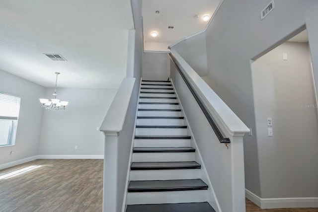 staircase with an inviting chandelier and wood-type flooring