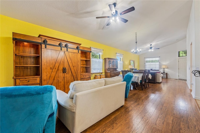 living room featuring ceiling fan with notable chandelier, a barn door, dark wood-type flooring, and vaulted ceiling