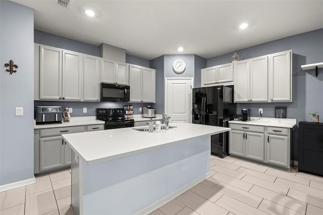 kitchen featuring sink, an island with sink, gray cabinets, and black appliances