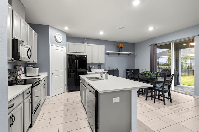 kitchen with a kitchen island with sink, black appliances, white cabinets, sink, and light tile patterned floors