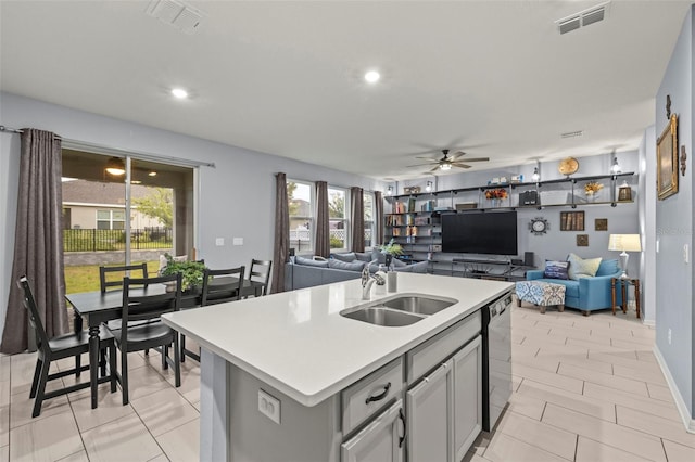 kitchen featuring ceiling fan, sink, black dishwasher, gray cabinets, and an island with sink