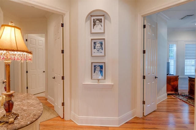 corridor with light hardwood / wood-style flooring and ornamental molding