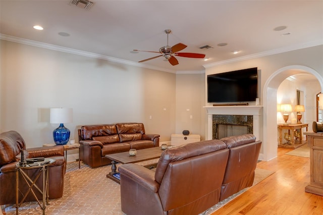 living room with ceiling fan, a fireplace, light hardwood / wood-style floors, and ornamental molding