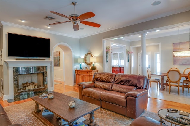 living room featuring ceiling fan, light hardwood / wood-style floors, crown molding, and a high end fireplace