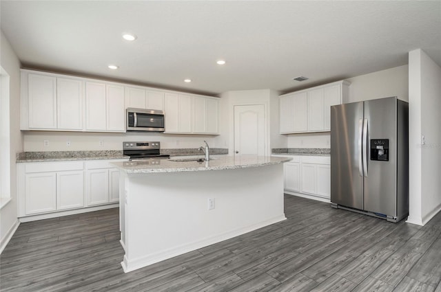 kitchen with appliances with stainless steel finishes, white cabinets, dark wood-type flooring, light stone counters, and a center island with sink