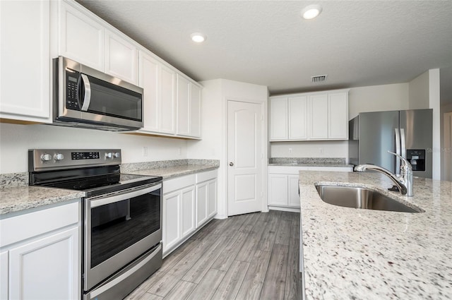 kitchen with white cabinets, appliances with stainless steel finishes, a textured ceiling, light hardwood / wood-style flooring, and sink