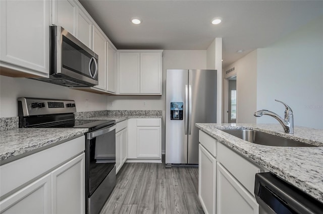 kitchen with sink, white cabinets, appliances with stainless steel finishes, light stone counters, and light hardwood / wood-style floors