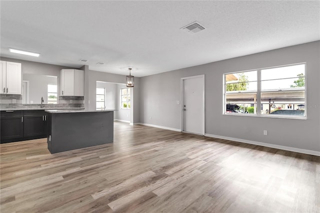 kitchen featuring light wood finished floors, light countertops, decorative backsplash, white cabinets, and a sink