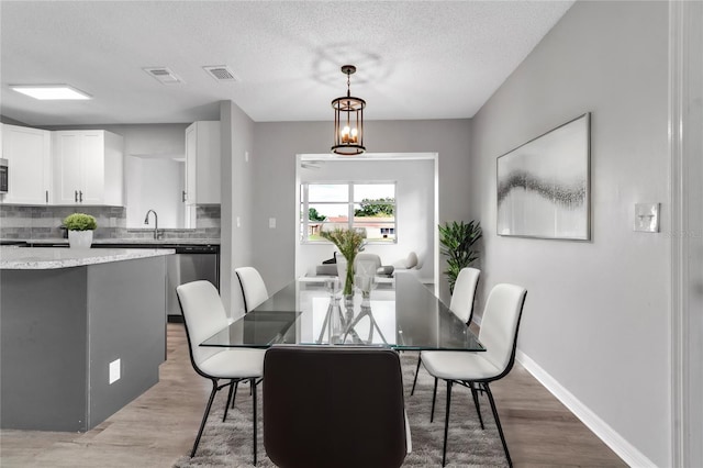 dining space with visible vents, an inviting chandelier, light wood-style floors, a textured ceiling, and baseboards