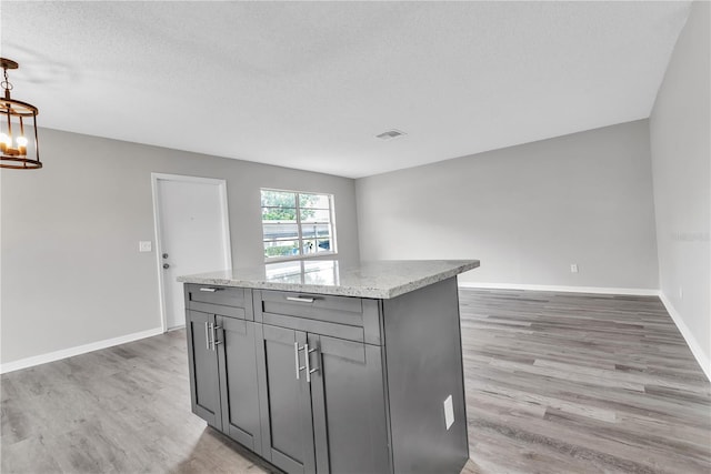 kitchen with gray cabinetry, a kitchen island, visible vents, baseboards, and light wood-type flooring