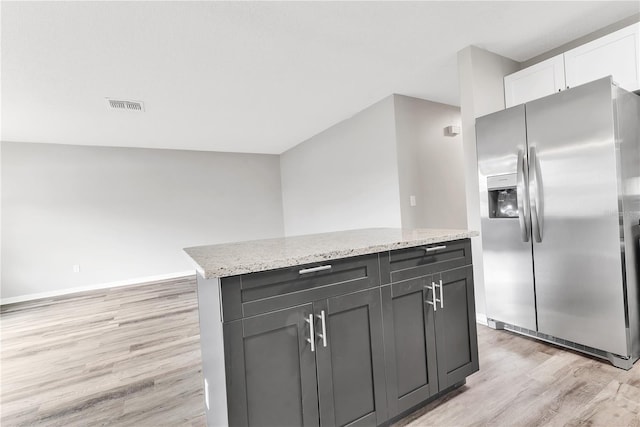 kitchen with visible vents, white cabinetry, light wood-type flooring, stainless steel refrigerator with ice dispenser, and light stone countertops