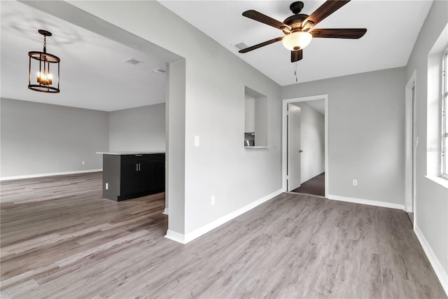 unfurnished room with baseboards, visible vents, wood finished floors, and ceiling fan with notable chandelier