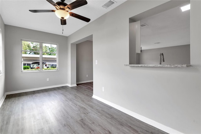 empty room with visible vents, ceiling fan, a sink, wood finished floors, and baseboards