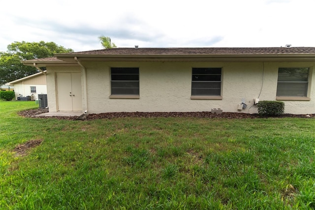 view of side of home with central AC unit, a lawn, and stucco siding