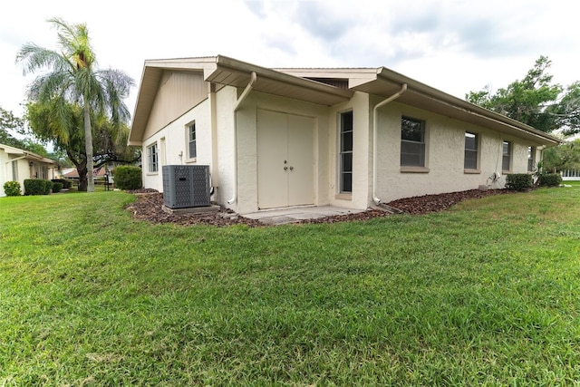 view of side of home featuring cooling unit, a yard, and stucco siding