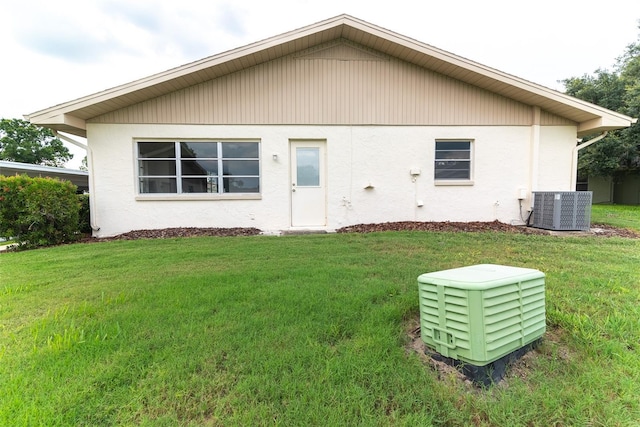 rear view of house with central air condition unit, stucco siding, and a yard