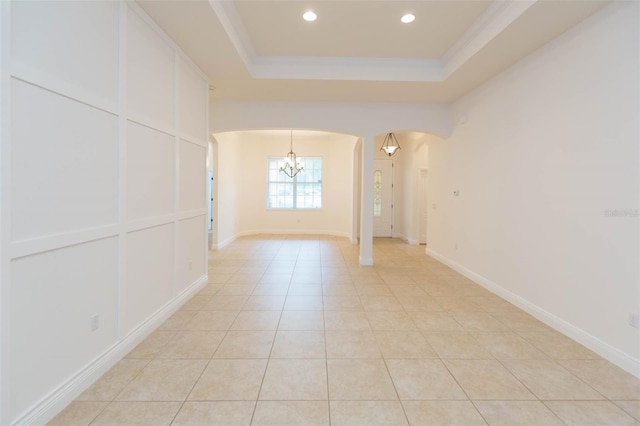 spare room with light tile patterned floors, a tray ceiling, an inviting chandelier, and crown molding