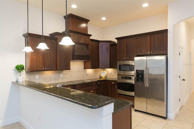 kitchen featuring custom exhaust hood, dark stone countertops, appliances with stainless steel finishes, decorative light fixtures, and kitchen peninsula