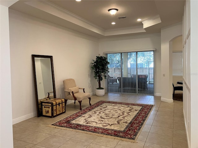 living area with light tile patterned flooring, ornamental molding, and a tray ceiling