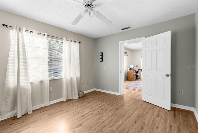 unfurnished room with a textured ceiling, light wood-type flooring, and ceiling fan