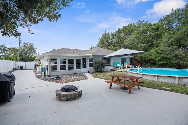 back of property with a fire pit, a sunroom, a fenced in pool, and a patio