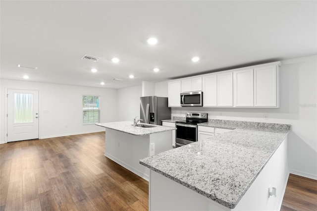 kitchen featuring stainless steel appliances, light stone counters, dark hardwood / wood-style floors, a center island with sink, and white cabinets