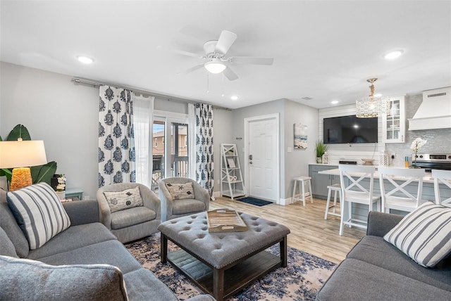 living room with ceiling fan with notable chandelier and light hardwood / wood-style floors