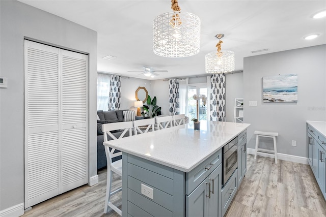 kitchen with light hardwood / wood-style flooring, hanging light fixtures, a center island, stainless steel microwave, and a kitchen bar