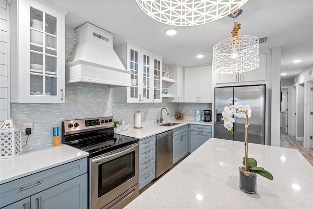 kitchen with decorative light fixtures, sink, white cabinets, stainless steel appliances, and custom range hood