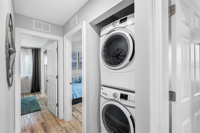 clothes washing area with stacked washer / drying machine and light wood-type flooring