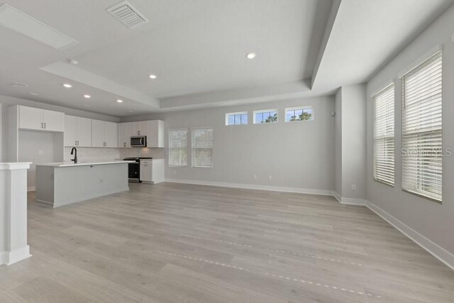 unfurnished living room featuring a raised ceiling, sink, and light wood-type flooring