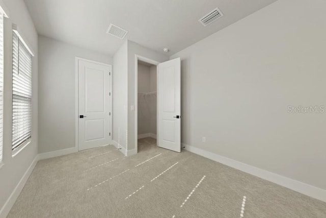 unfurnished bedroom with light carpet, a walk in closet, and a closet