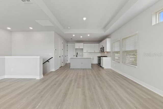 unfurnished living room featuring a tray ceiling and light hardwood / wood-style flooring