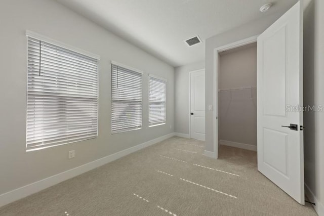 unfurnished bedroom with a spacious closet, light colored carpet, and a closet